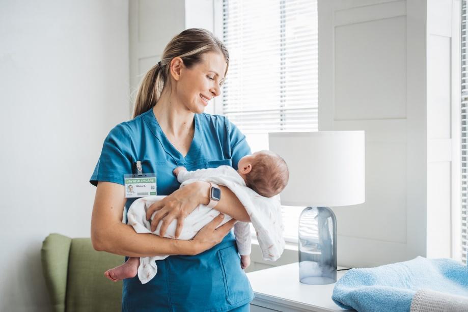 A person in blue scrubs holding a baby Description automatically generated